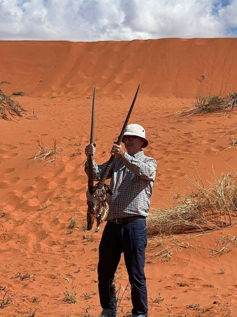 A guest on a red dune holding up a bleached oryx skull by its horns